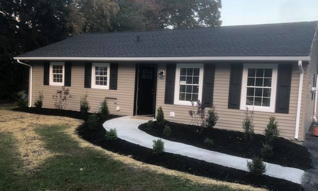 A house with black shutters and a walkway leading to it.