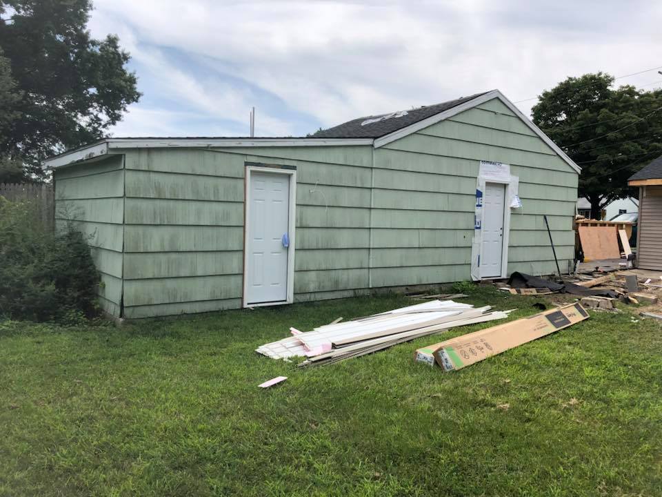 A green house with white doors is sitting in the grass.