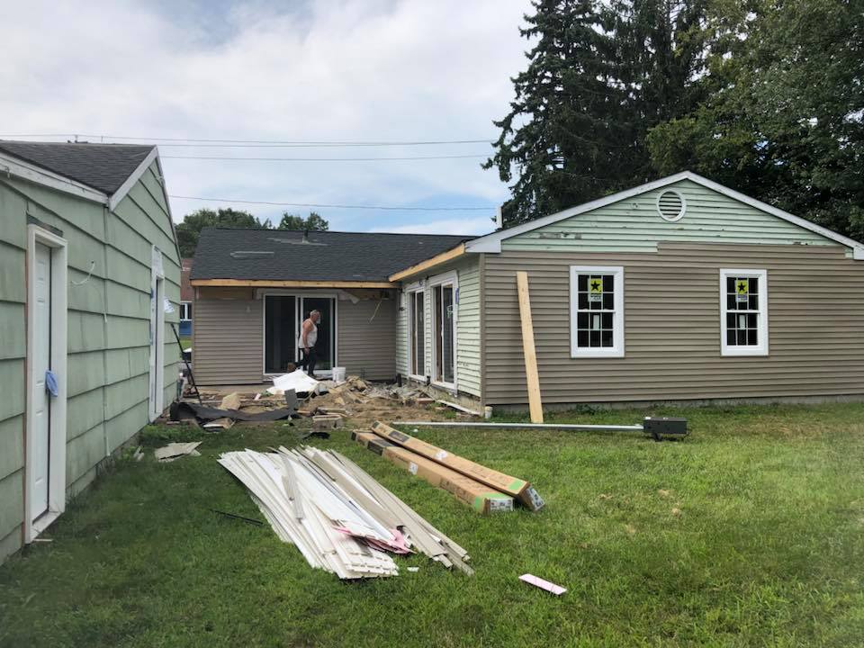 A house is being remodeled in a backyard with a lot of wood in the grass.