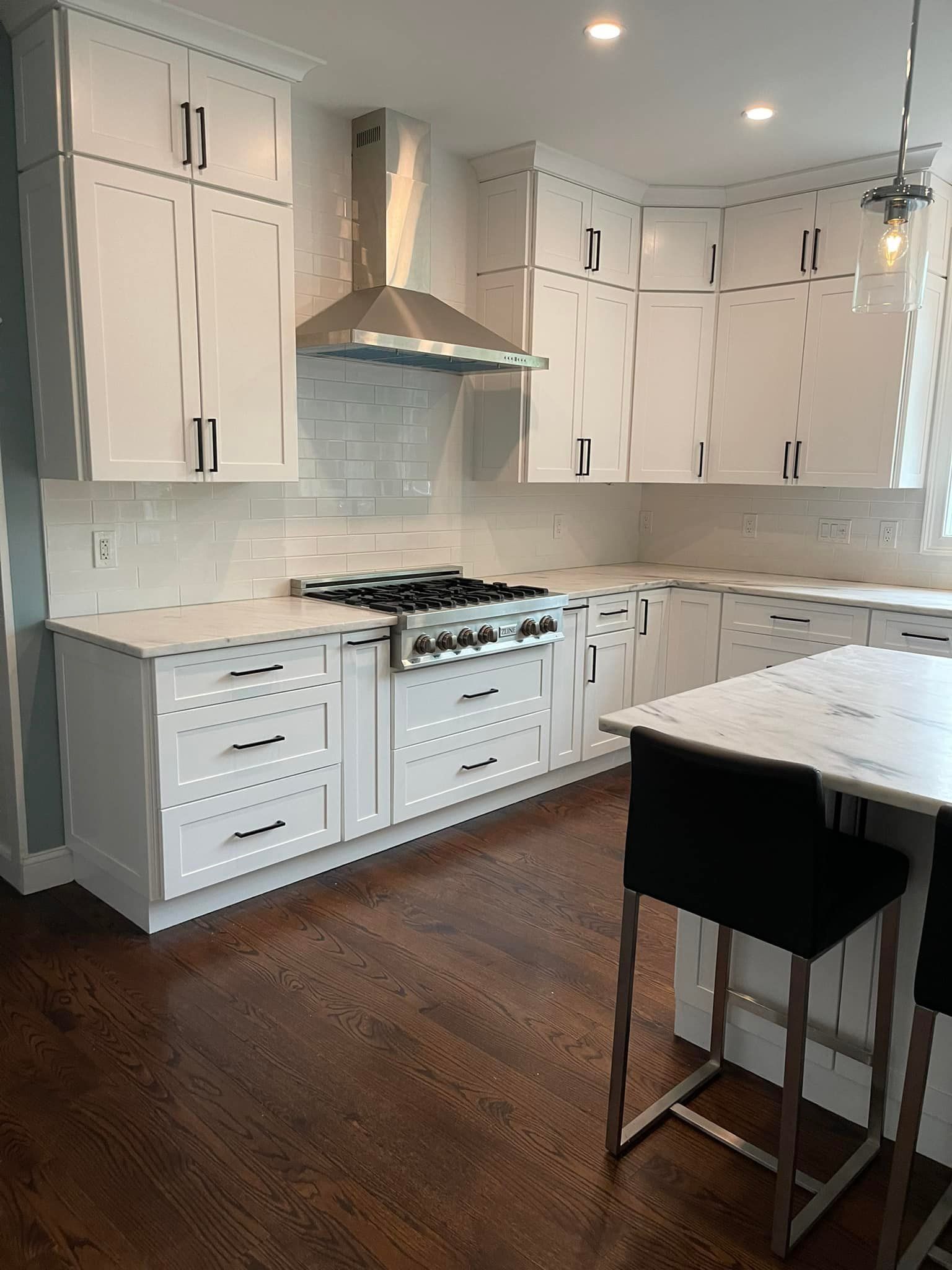 A kitchen with white cabinets , a stove , a table and chairs.