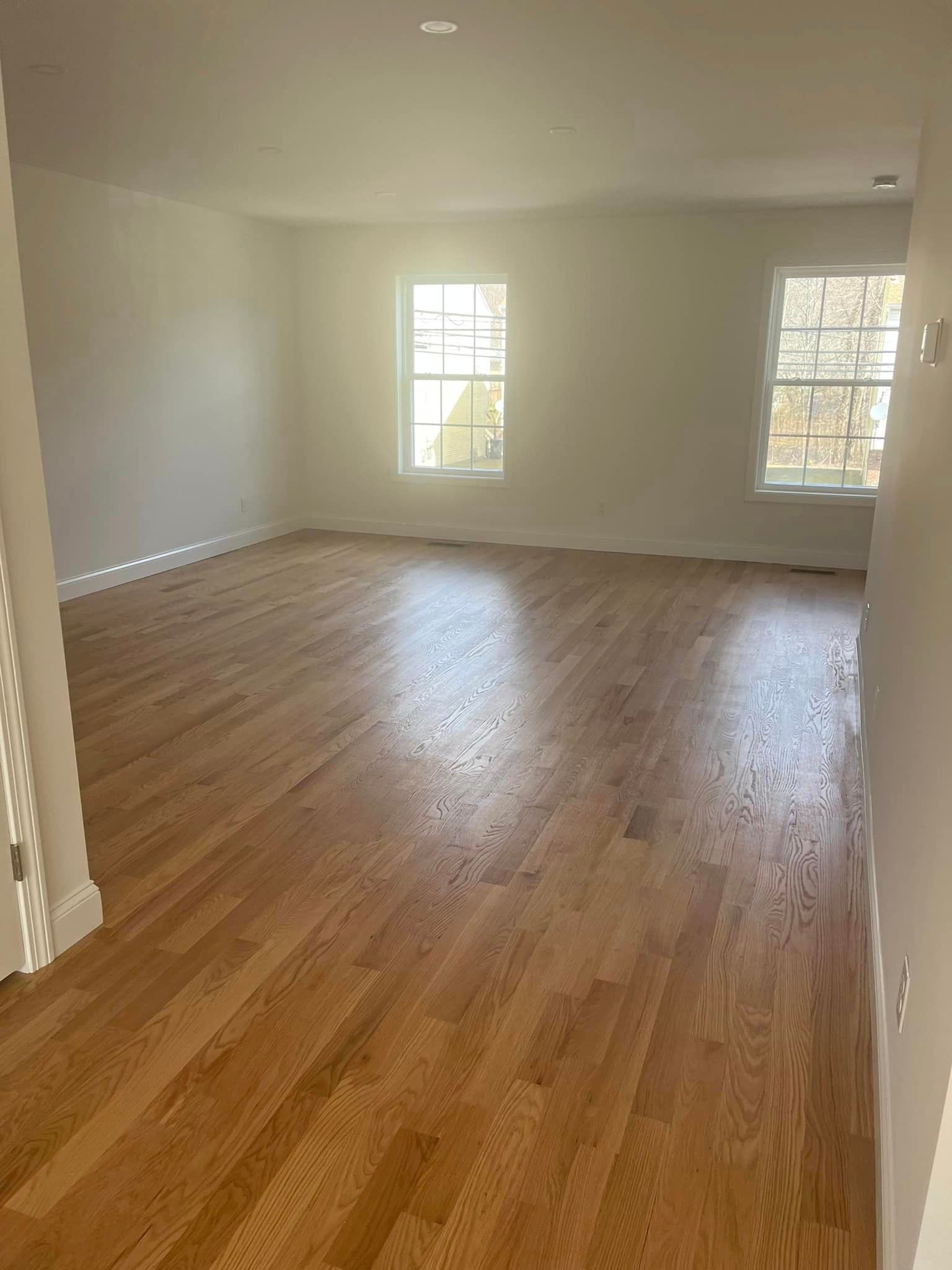 An empty living room with hardwood floors and two windows.