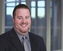 A man in a suit and tie is smiling in front of a window.