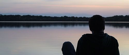 A person is sitting on the shore of a lake looking at the water.