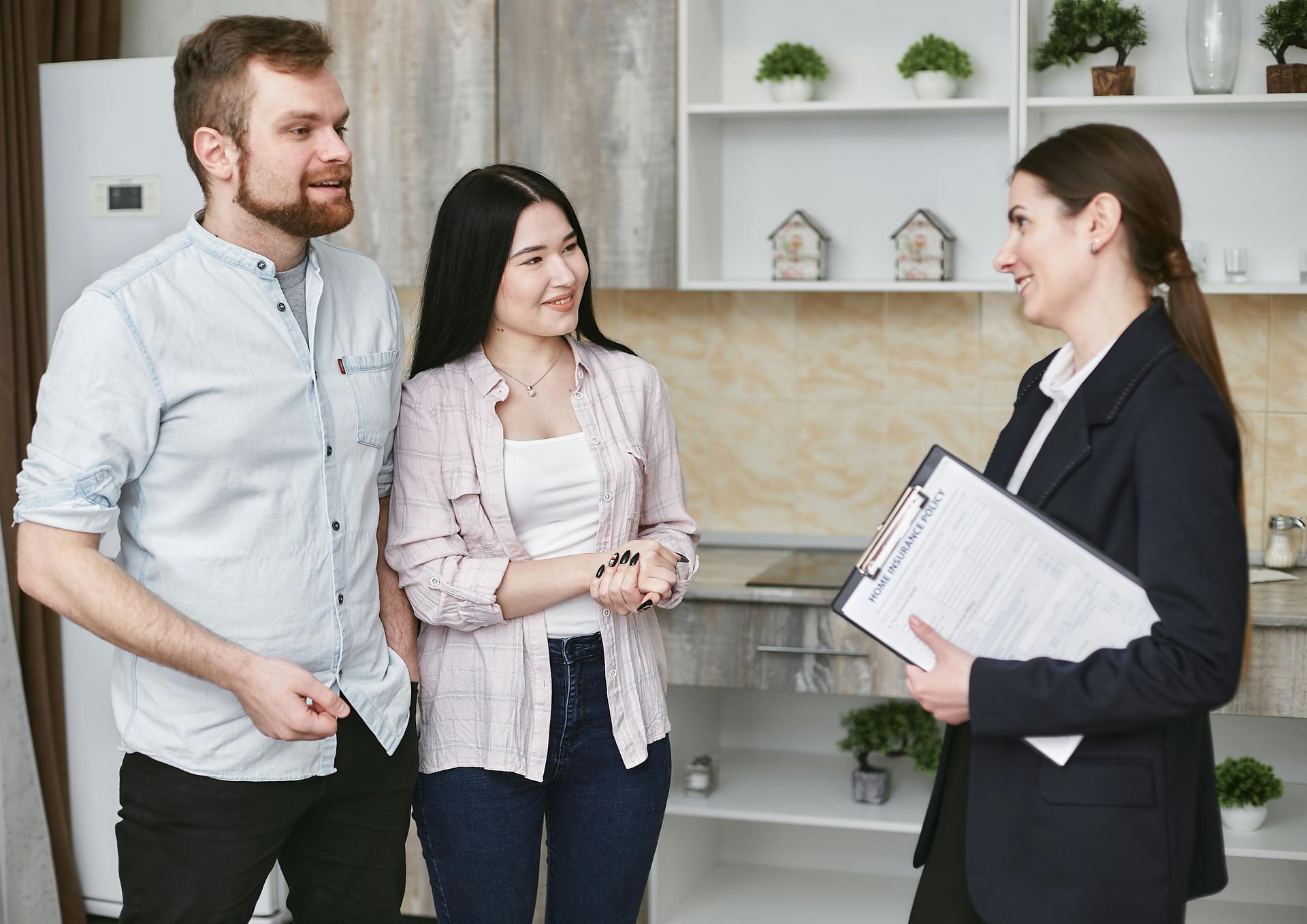 A man and a woman are shaking hands with a real estate agent in a kitchen.