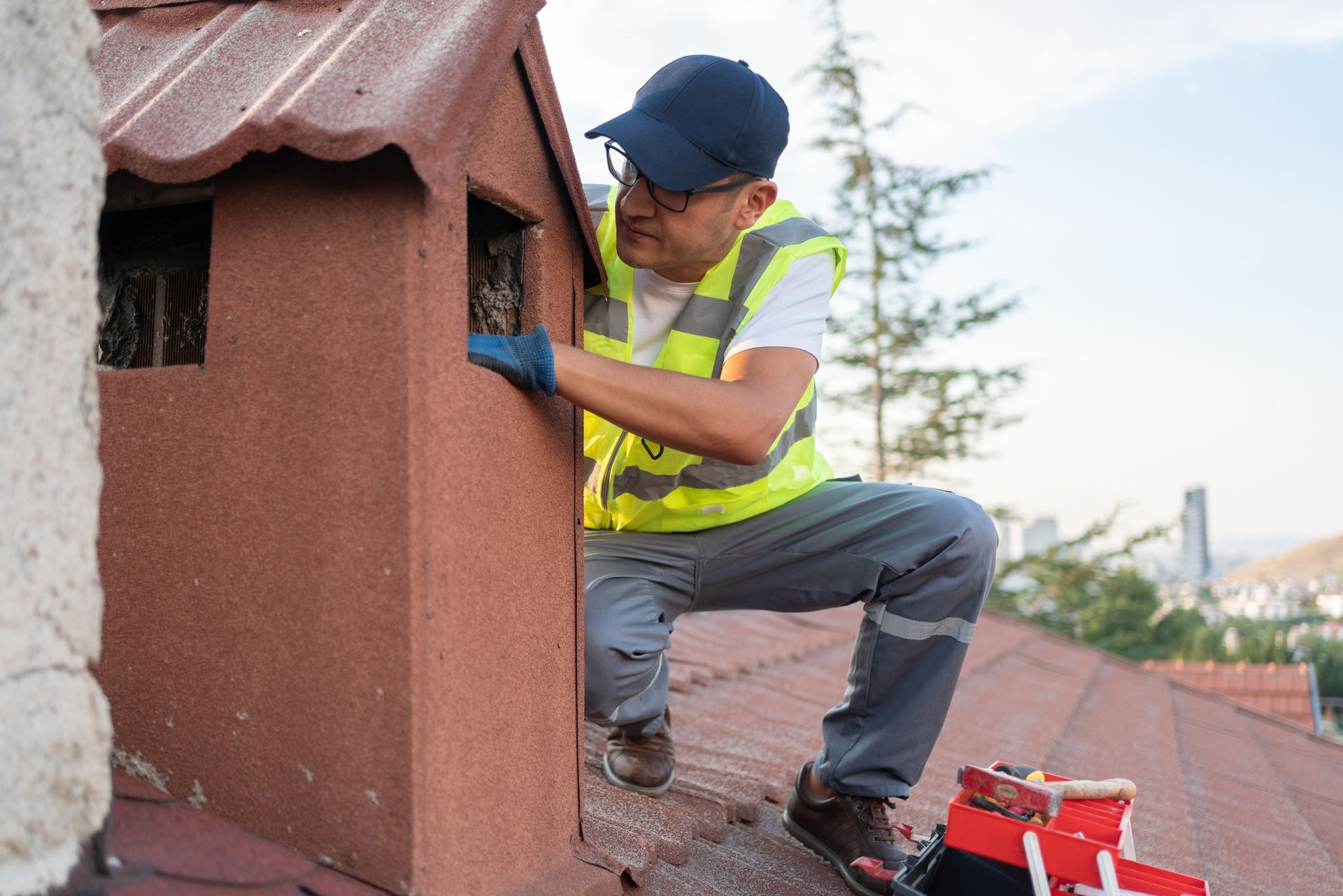 A man is kneeling on top of a roof fixing a chimney.