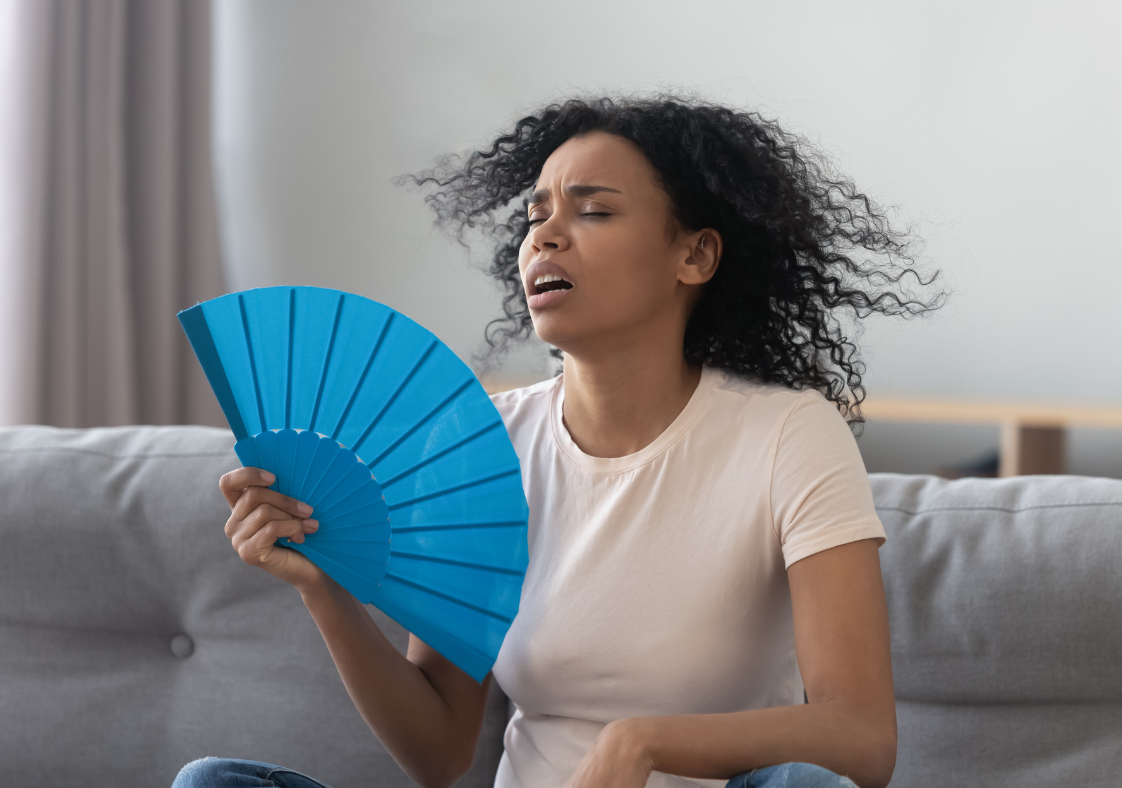 A woman is sitting on a couch holding a blue fan because central air unit went out