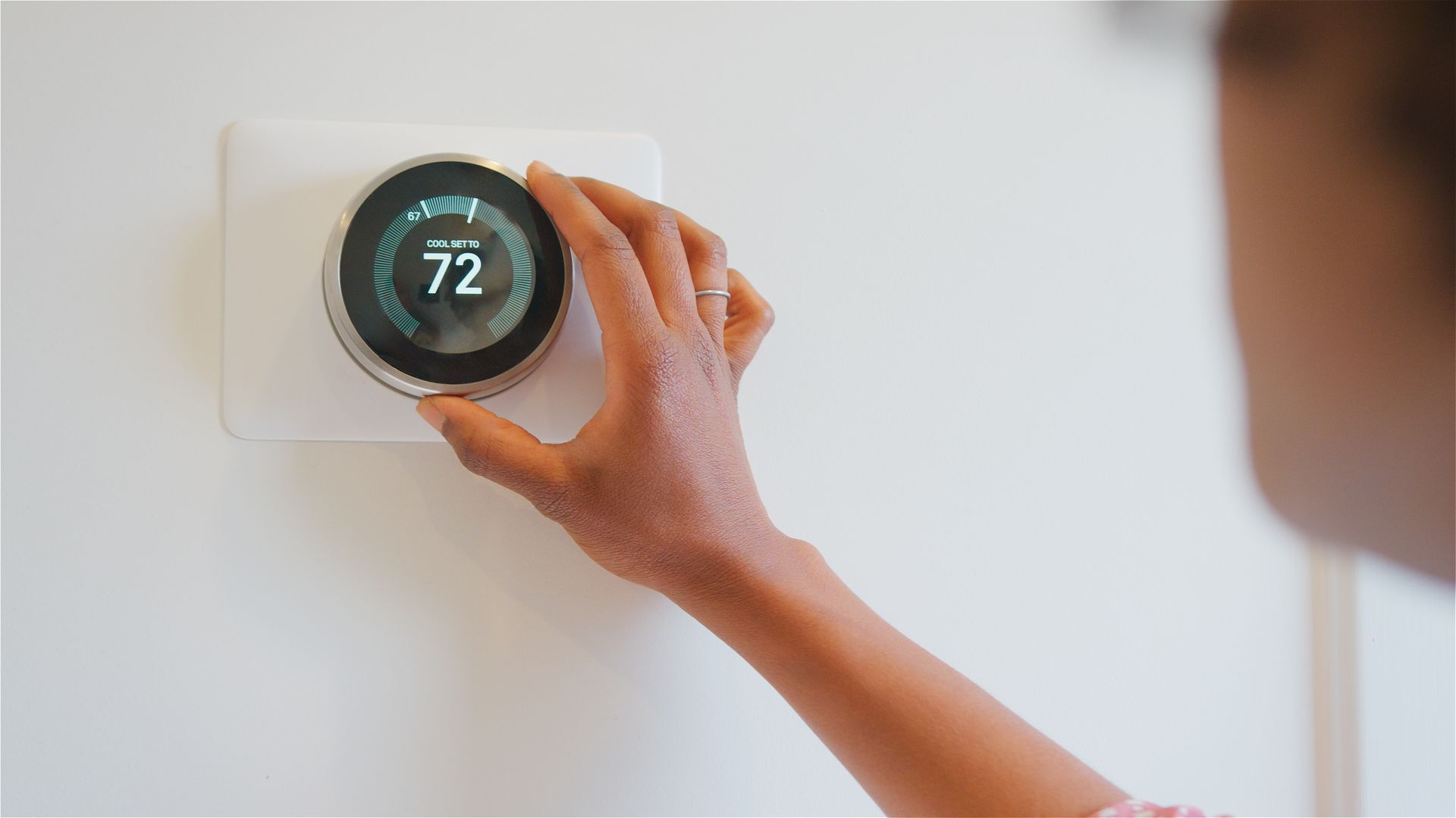 Person adjusting a smart thermostat set to 72 degrees.
