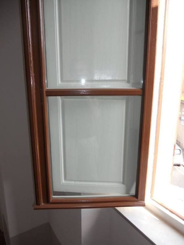 Finestra con cornice marrone e persiane verde chiaro chiuse, accanto a una finestra aperta.