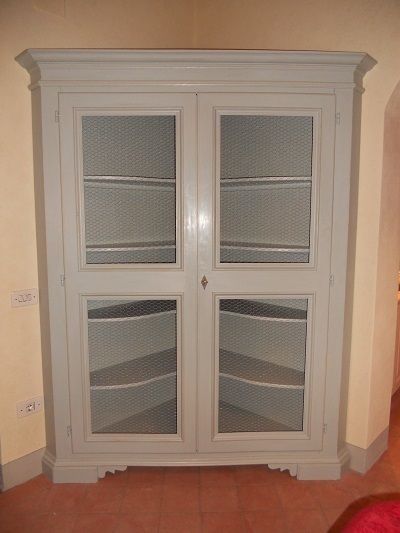 Mobile angolare verniciato grigio con ante in vetro e rete metallica.