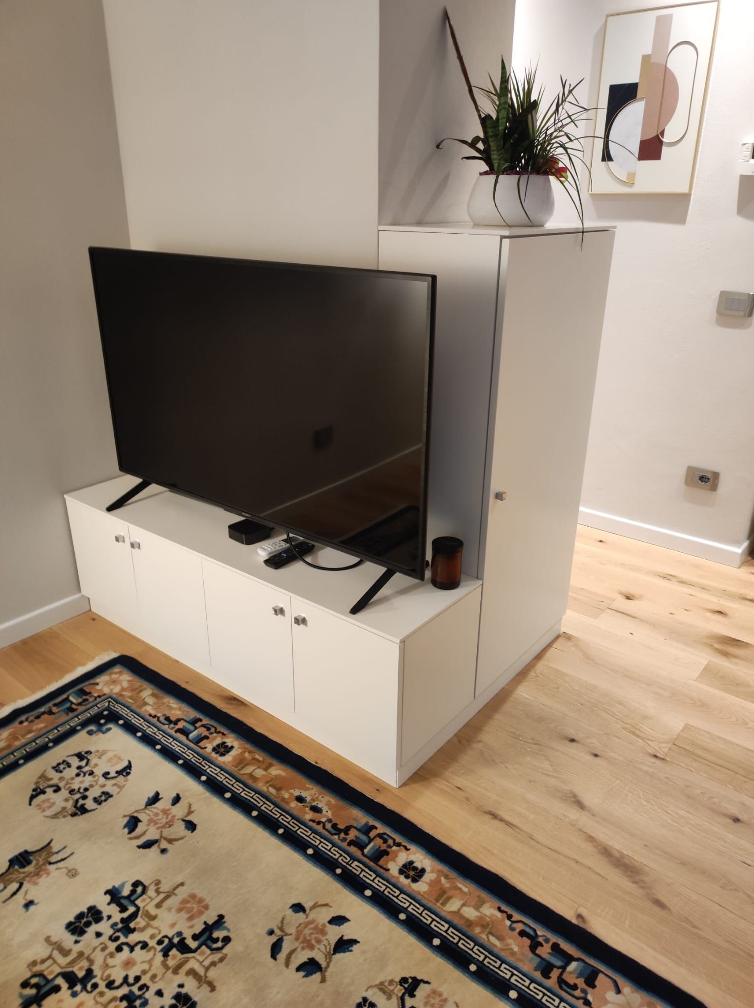 Un moderno mobile porta TV bianco con un televisore nero montato, un tappeto e un pavimento in legno.