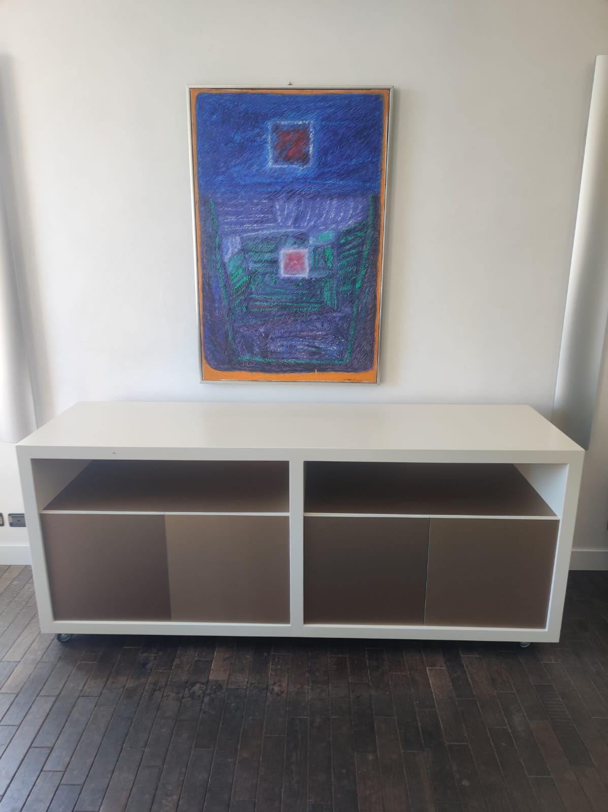 Mobile multimediale bianco con ante marroni sotto un'opera d'arte astratta blu su parete bianca.