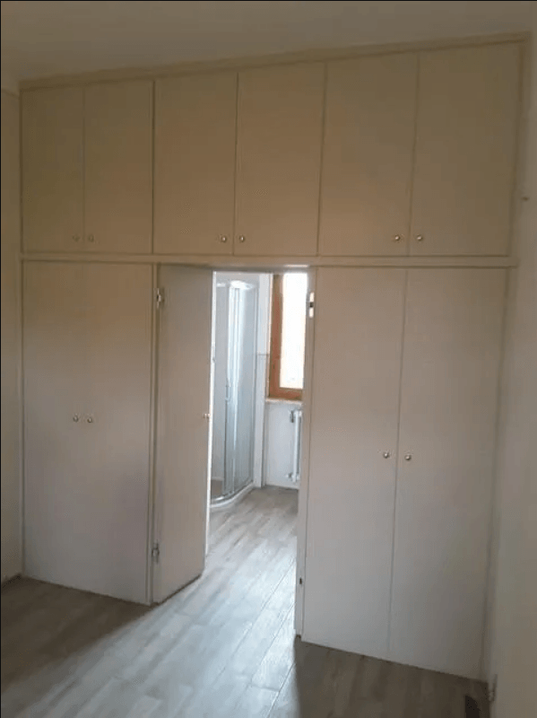 Armadietti bianchi a muro sopra e accanto alla porta di un bagno con doccia.