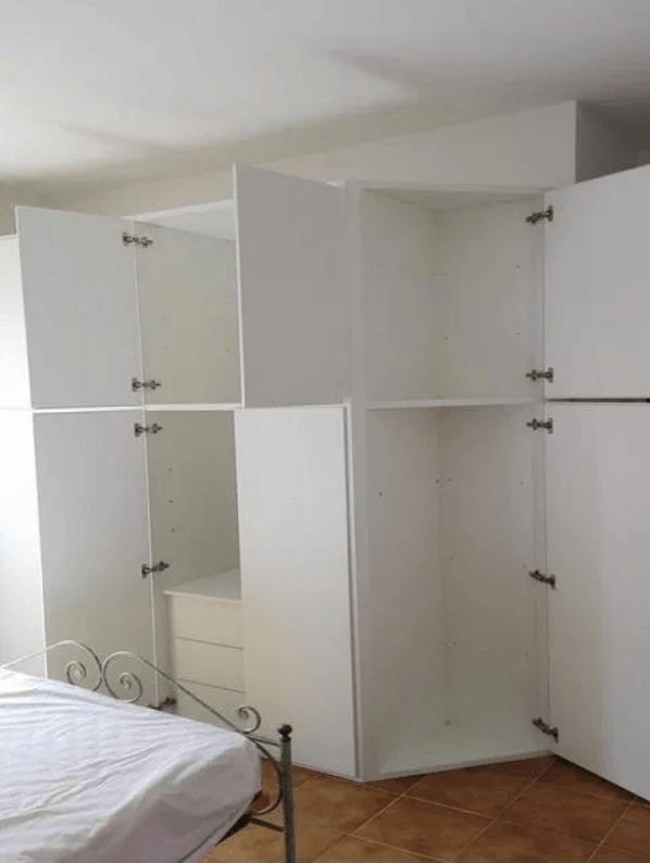 Ante bianche dell'armadio aperte, che rivelano ripiani e cassetti vuoti. Ambiente della camera da letto.