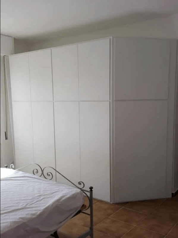 Armadio bianco a muro in una camera da letto, con un letto in primo piano e pavimento piastrellato.