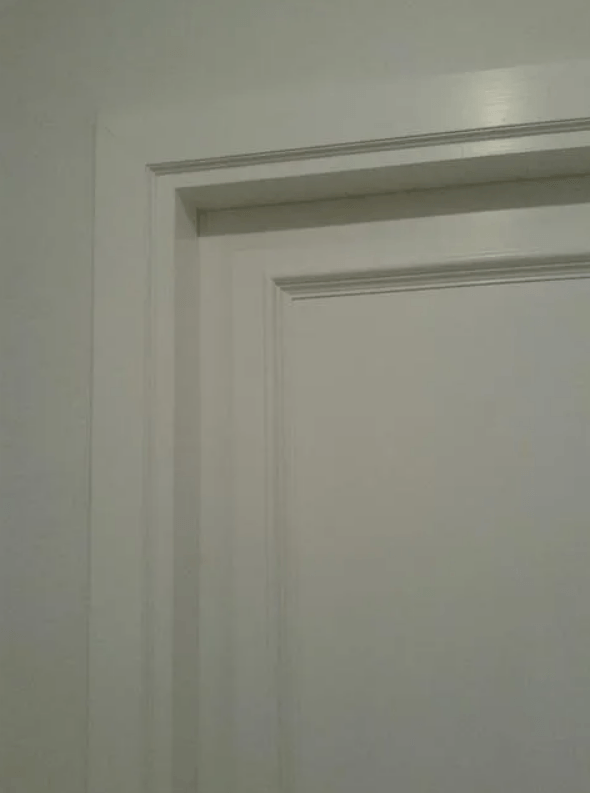 Telaio della porta bianco con modanature a strati contro una parete bianca.