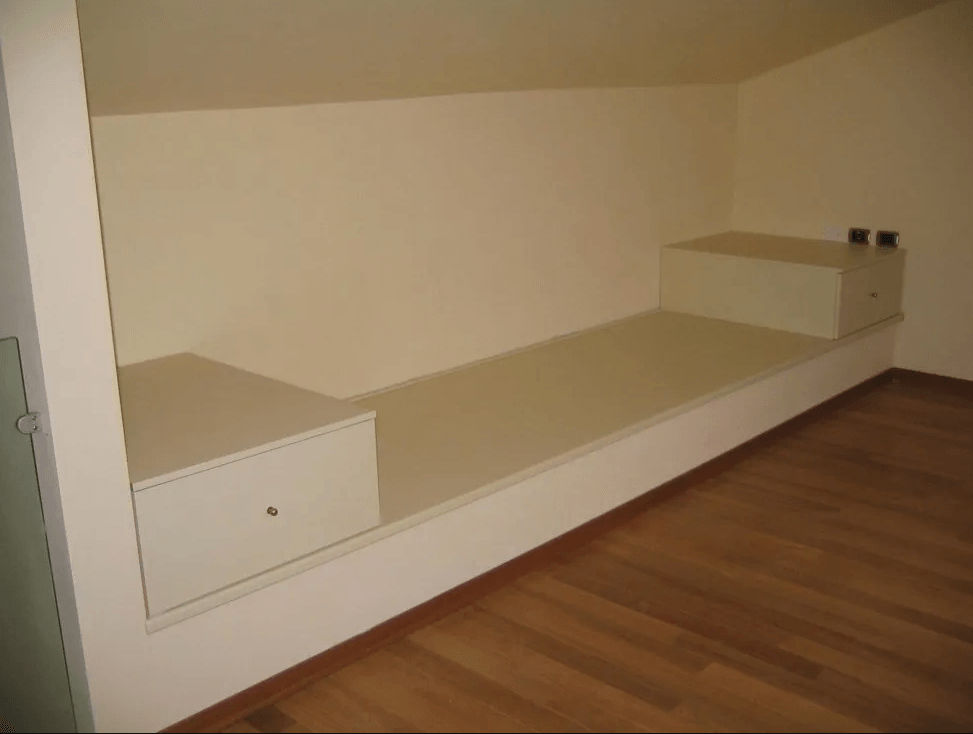 Panca beige integrata con due contenitori in una mansarda con pavimento in legno.