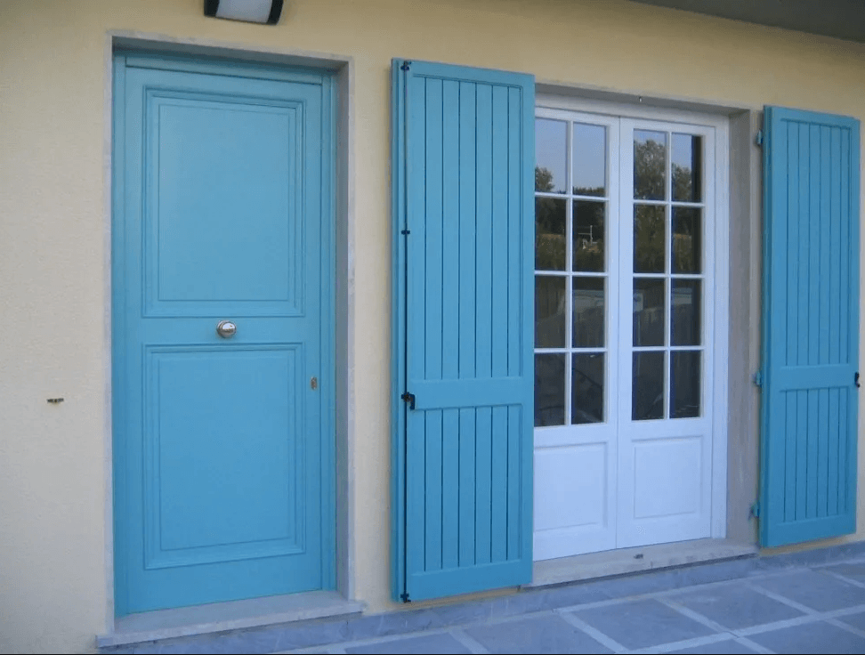 Porta e persiane blu su una porta a vetri con cornice bianca contro una parete giallo pallido.