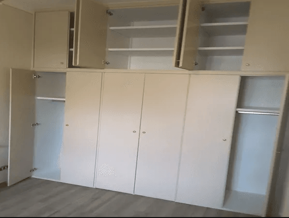 Armadio bianco a muro con più ante e ripiani, alcuni dei quali aperti. Disposizione della stanza.