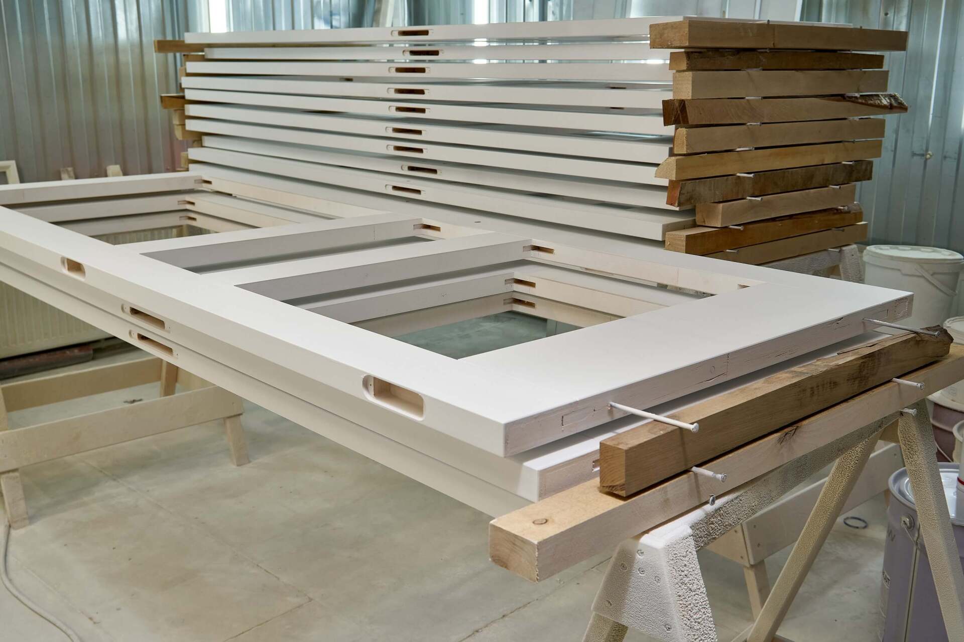 Telai di porte bianche impilati, con pezzi di legno aggiuntivi. Spazio di lavoro di colore chiaro.