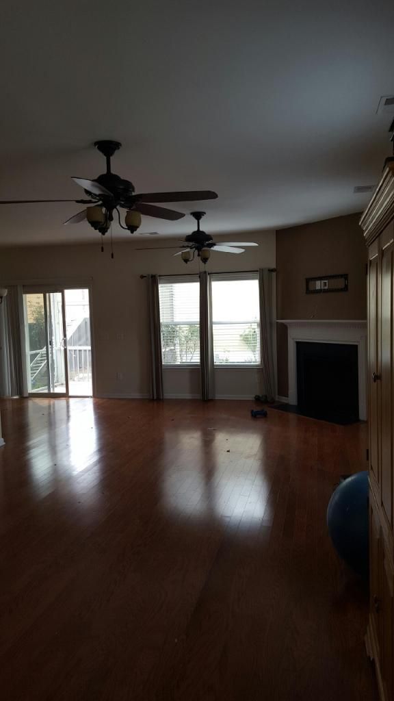 An empty living room with hardwood floors , ceiling fans , and a fireplace.