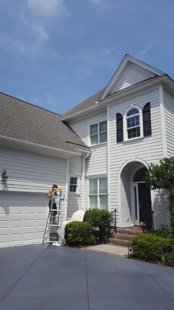 A man is standing on a ladder in front of a white house.
