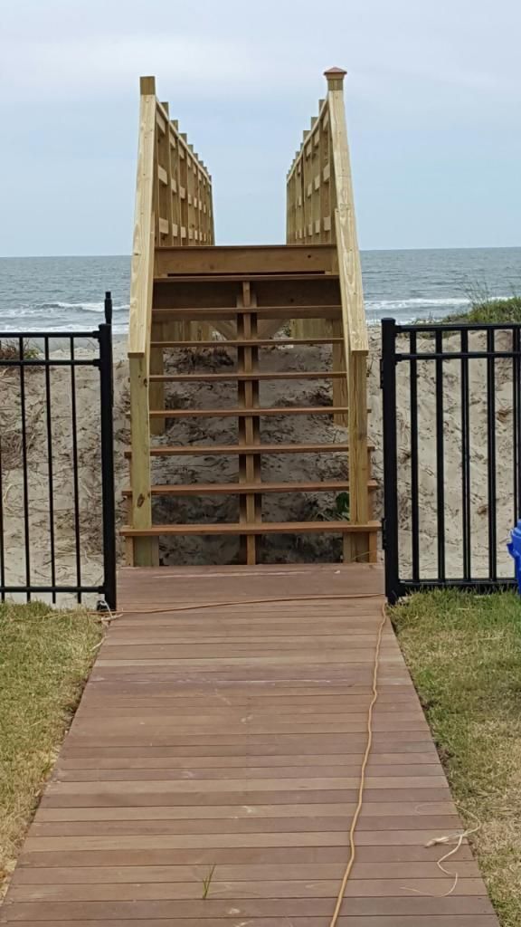 A wooden walkway leading to the beach with stairs leading up to the ocean.