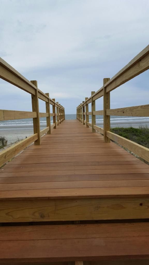 A wooden walkway leading to the ocean on a cloudy day.