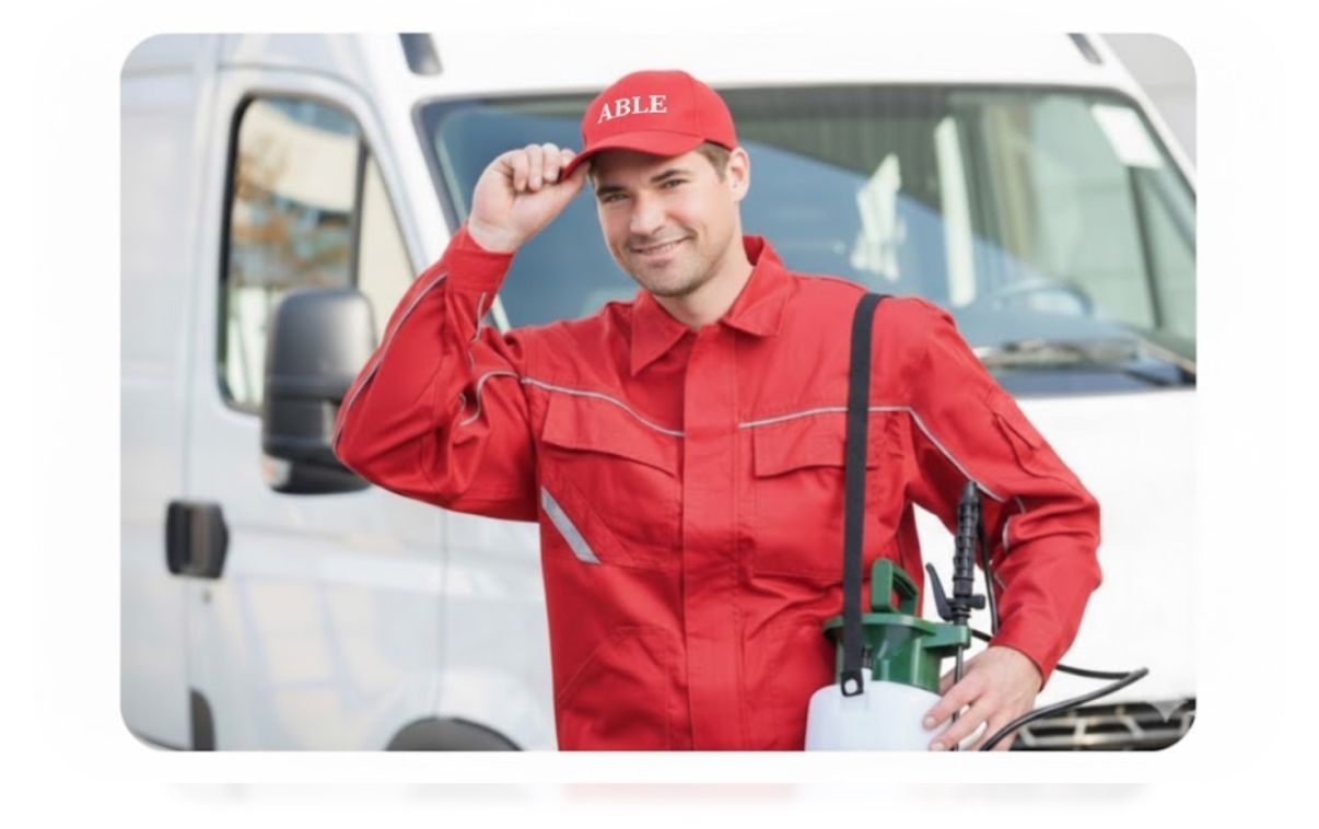 Man in red uniform and cap by a white van, holding a sprayer.