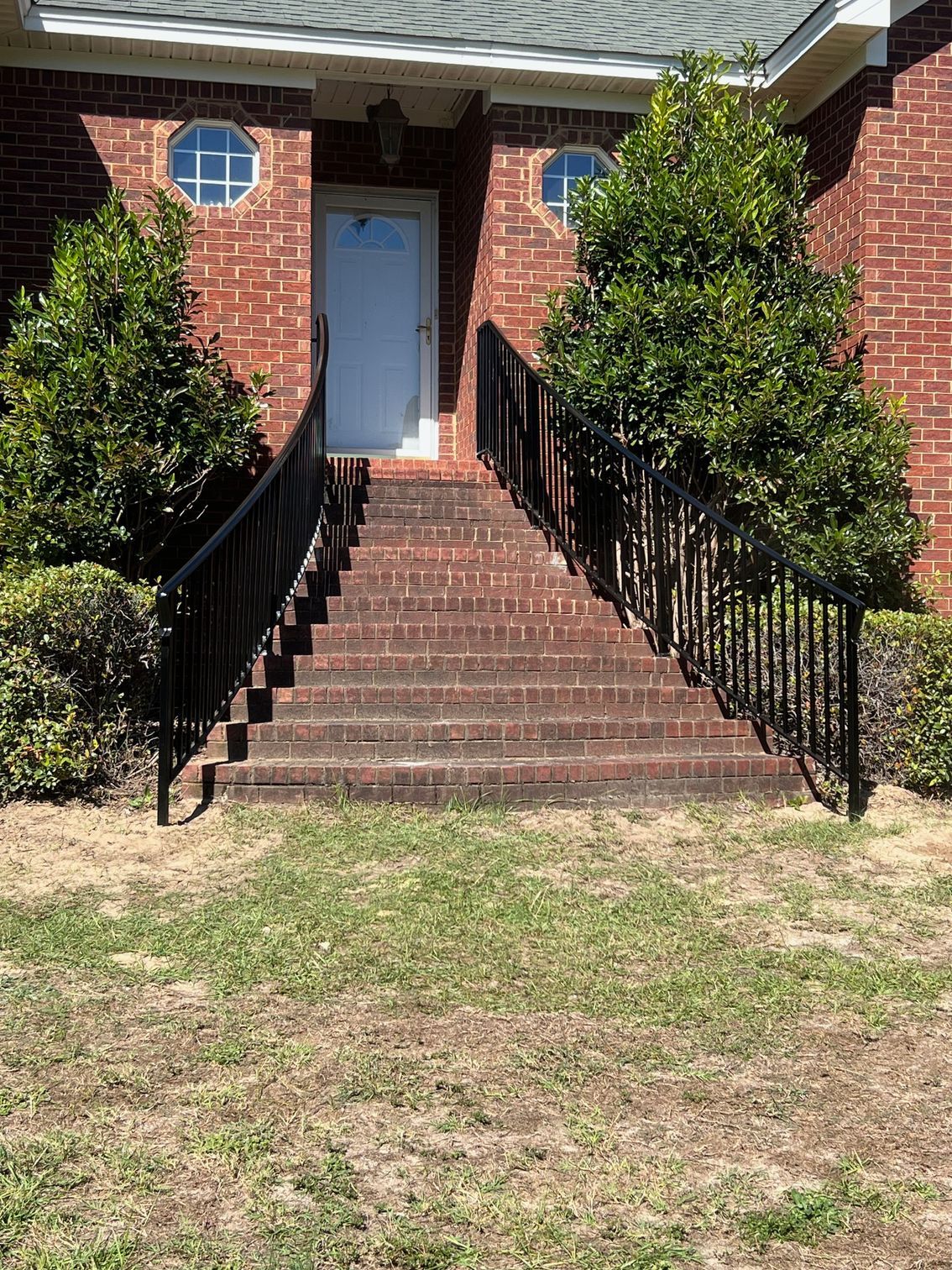 Brick steps leading to a white door, flanked by black railings and shrubs.