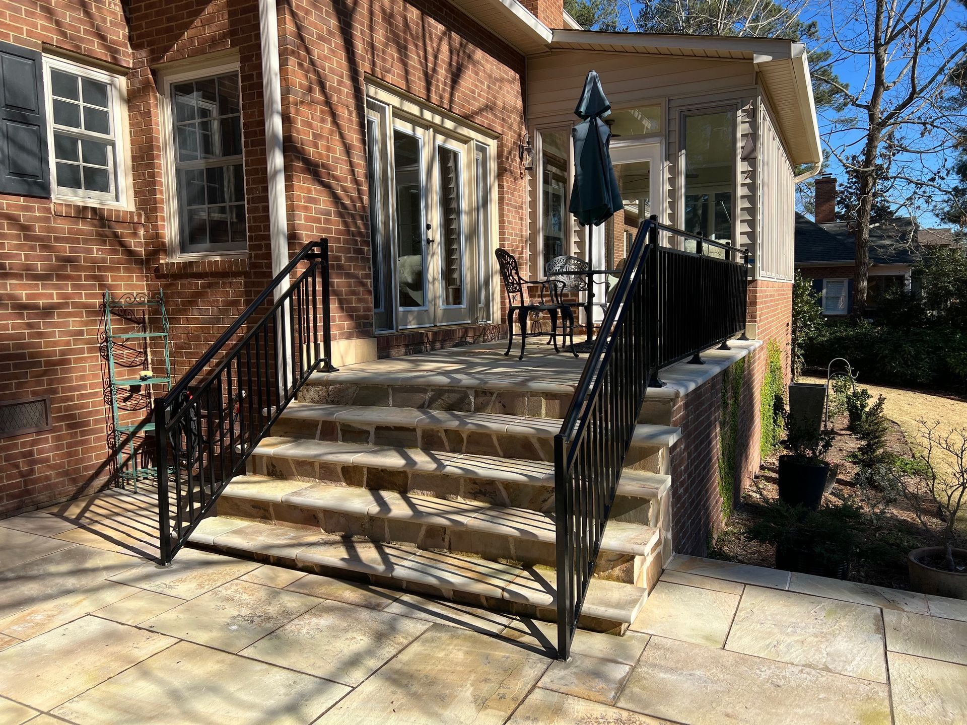 Brick home exterior with stone steps and black metal railings leading to a patio with a screened porch.