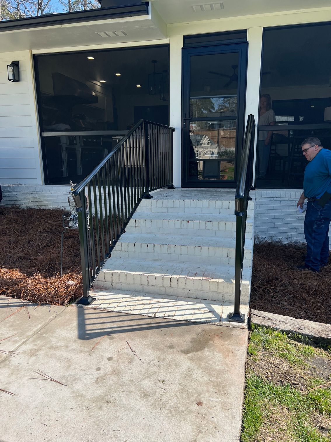 Black railing, steps, and entryway with a person on the right. White brick stairs, white siding.
