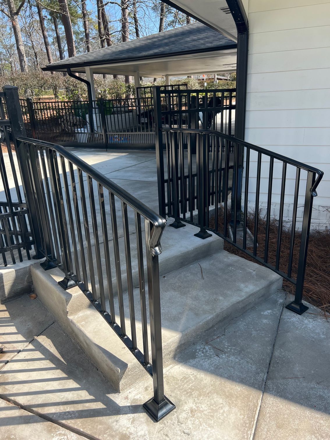 Black metal railing along concrete steps leading to a covered porch.