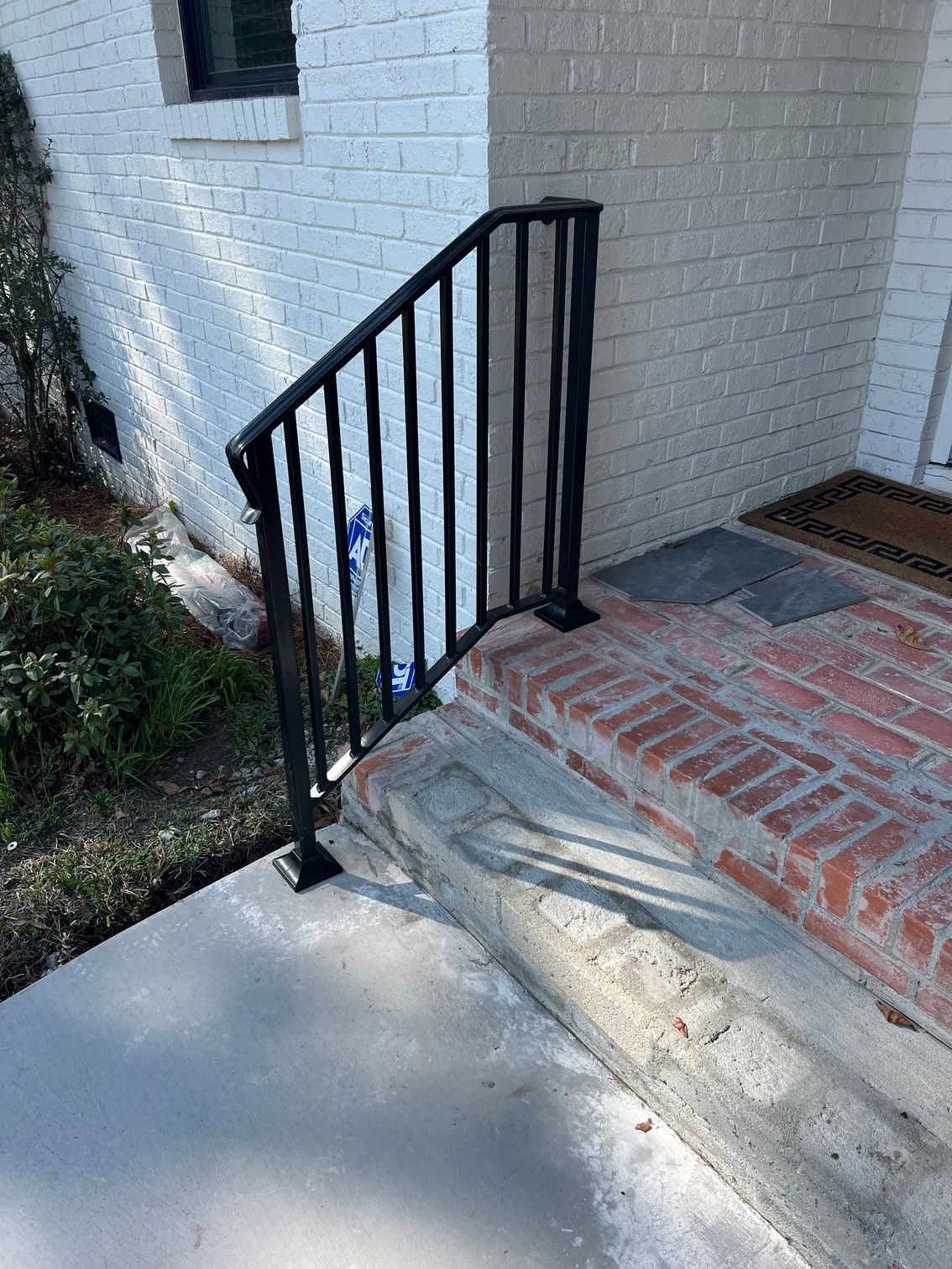 Black metal handrail on brick and concrete steps leading to a white brick building.