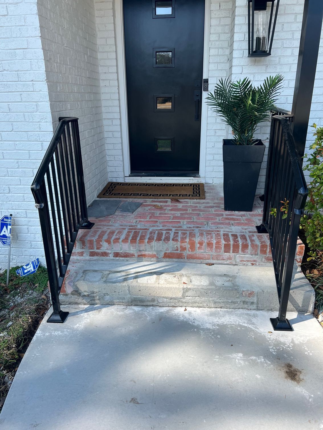 Black door with brick steps, concrete landing, and black metal handrails.
