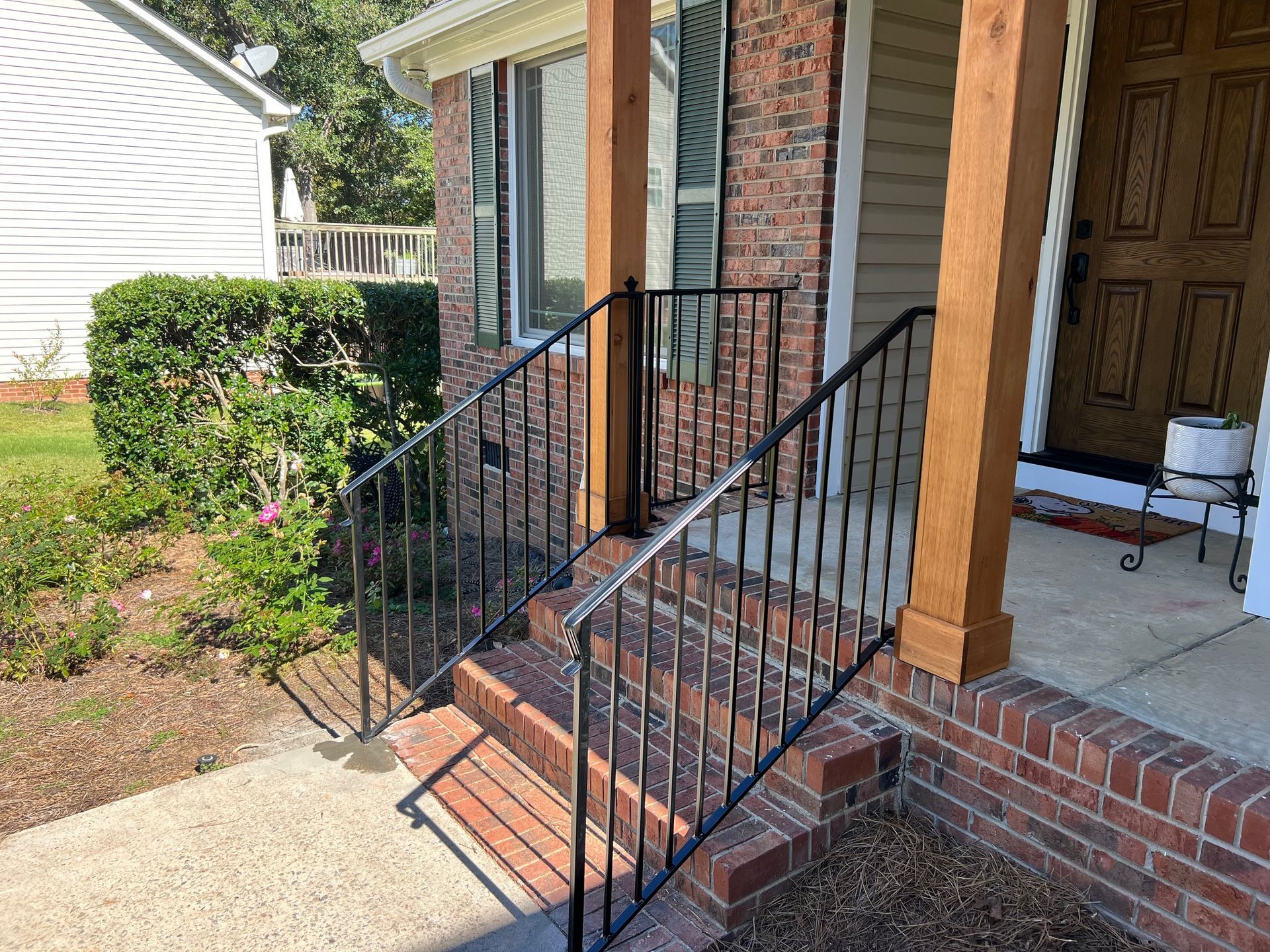 Black metal handrails on brick steps leading to a front door with wood columns and a small porch.