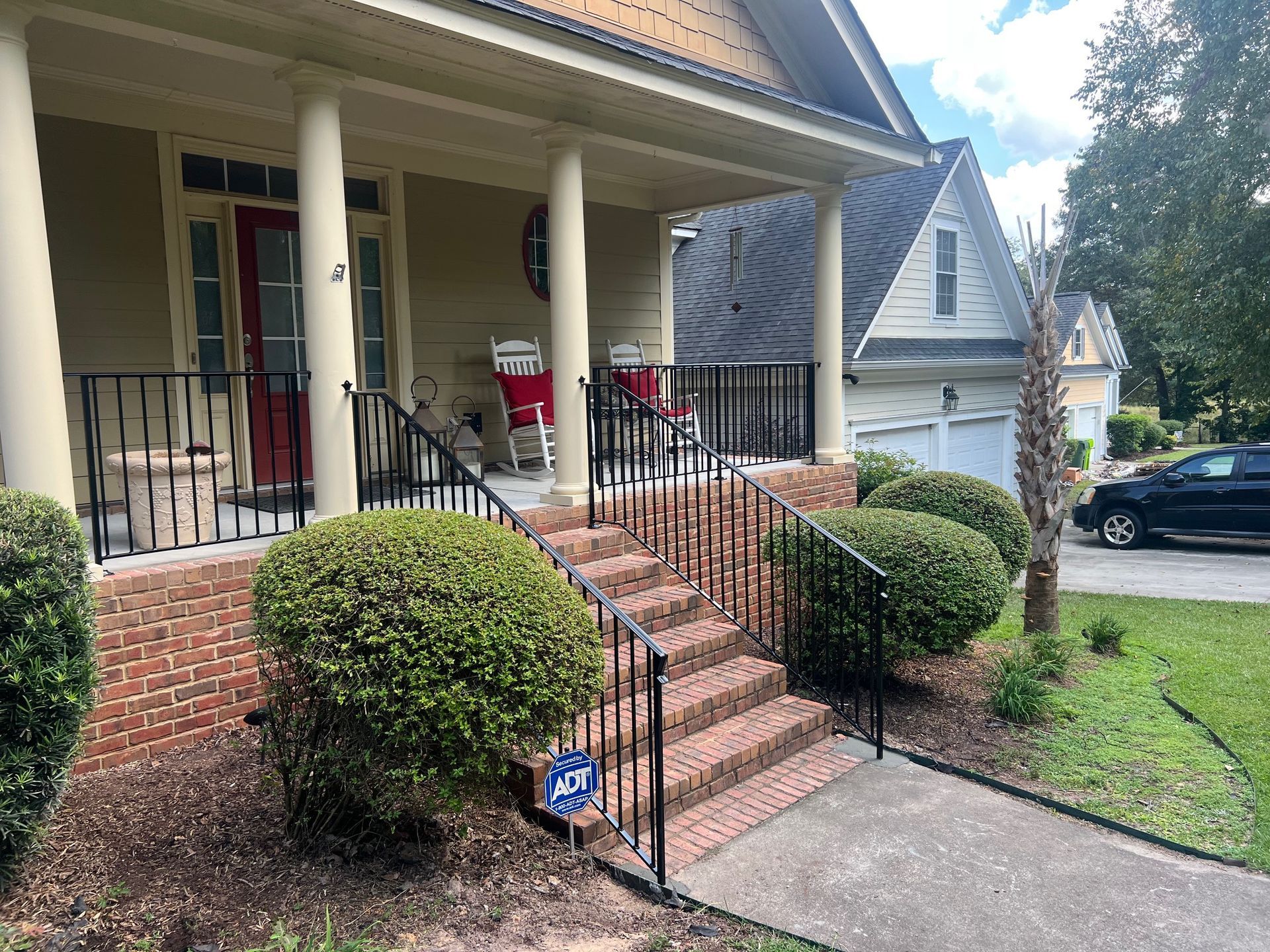 A house with a porch and steps, featuring brick, bushes, and a black railing.
