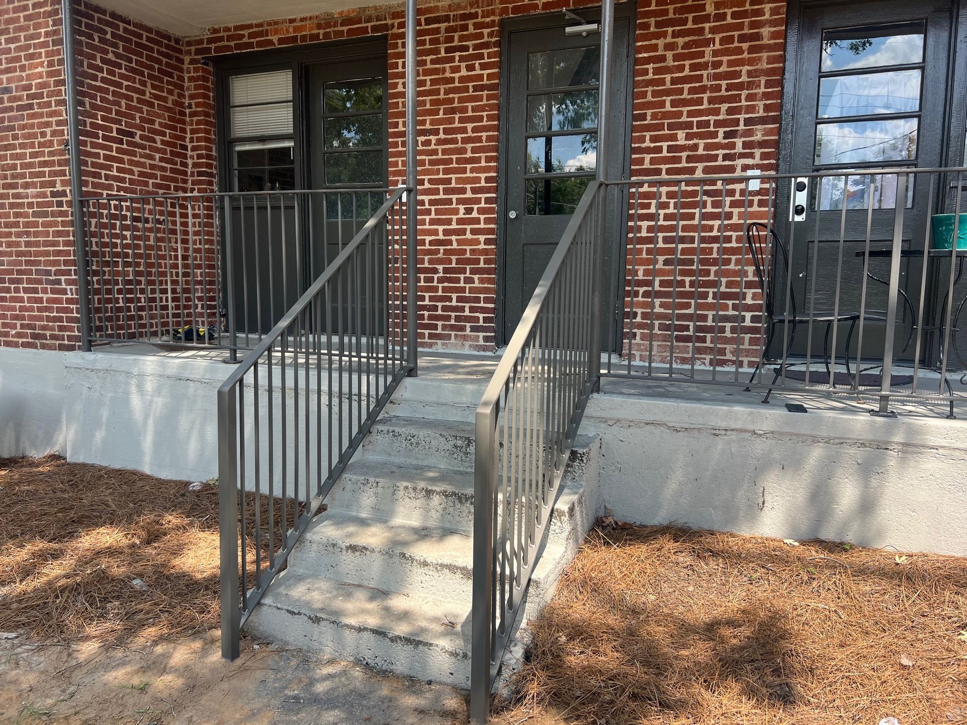 Exterior view of a brick building with a concrete stoop, metal railings, and dark doors.