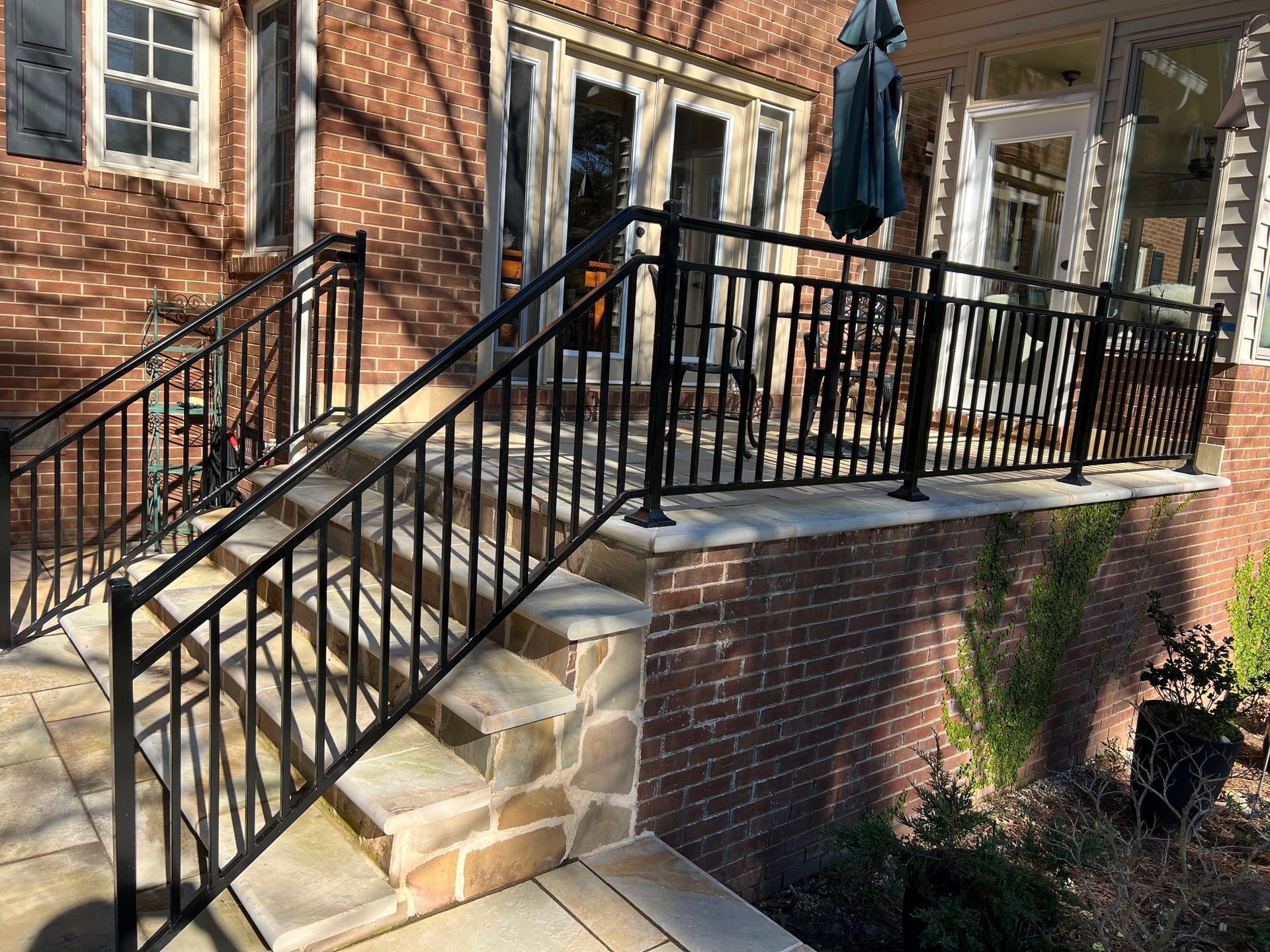 Black metal railings on brick steps leading to a porch with an umbrella.
