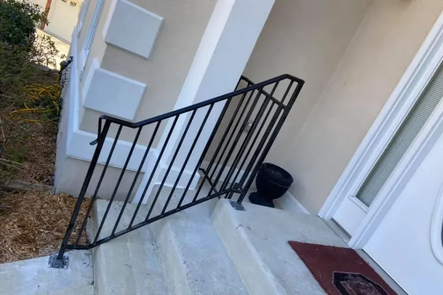 Black metal handrail on concrete steps leading to a building's entrance.