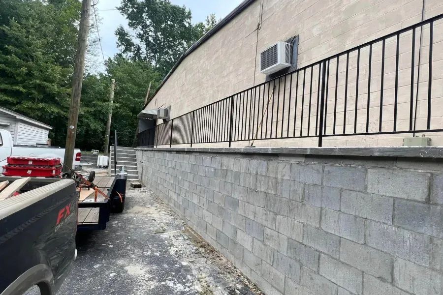 Exterior view of a building with a cinder block wall, black railing, and an AC unit.