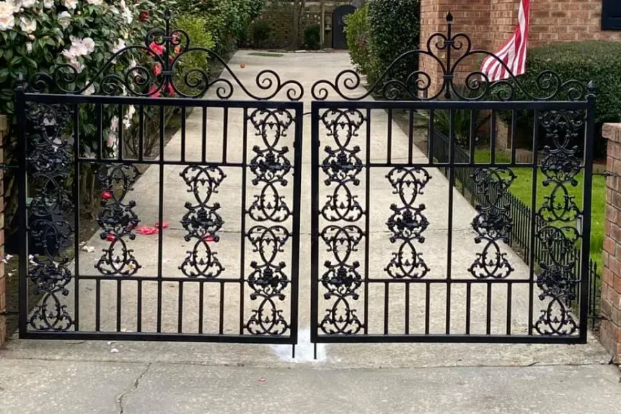 Black wrought iron gates, ornate scrollwork design, leading into a driveway.