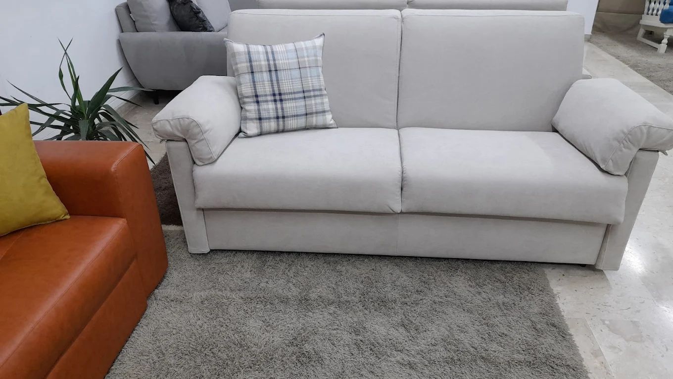 Divano beige con cuscino a quadri e poltrona in pelle arancione.