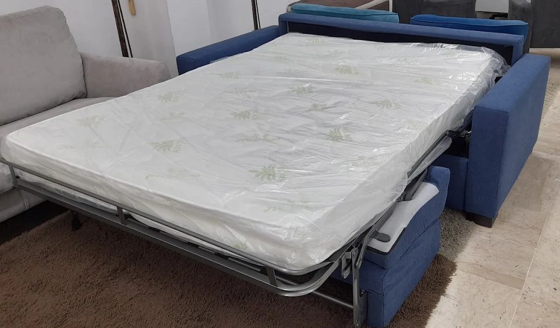 Divano letto blu, completamente allungato, con materasso bianco, su un tappeto.