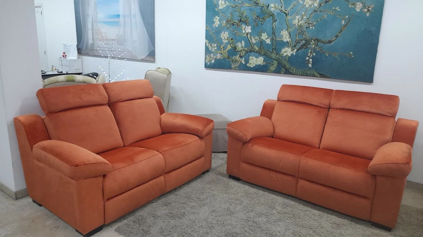 Due divani arancioni in una stanza, con opere d'arte alle pareti e un tappeto sul pavimento.