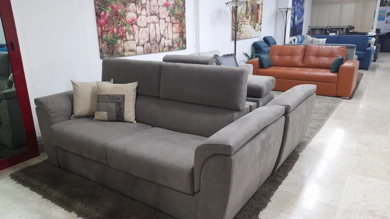 Divani grigi e marroni in un negozio di mobili, con cuscini decorativi e opere d'arte alle pareti.