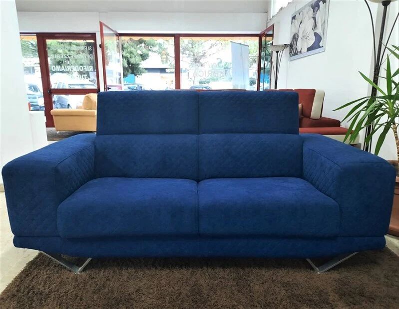Divano blu a due posti con schienale alto e gambe argentate, esposto in uno showroom.