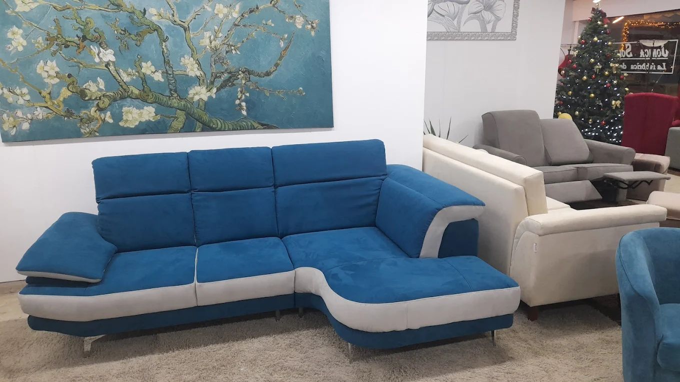 Divano componibile blu e grigio nello showroom di un negozio di mobili con un dipinto floreale e un albero di Natale.
