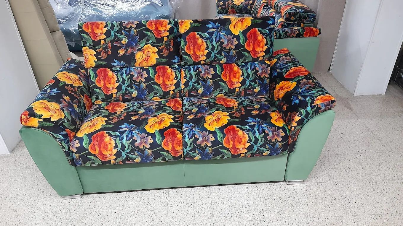 Divano a due posti con motivo floreale su sfondo nero, lati verdi e tappeto bianco.