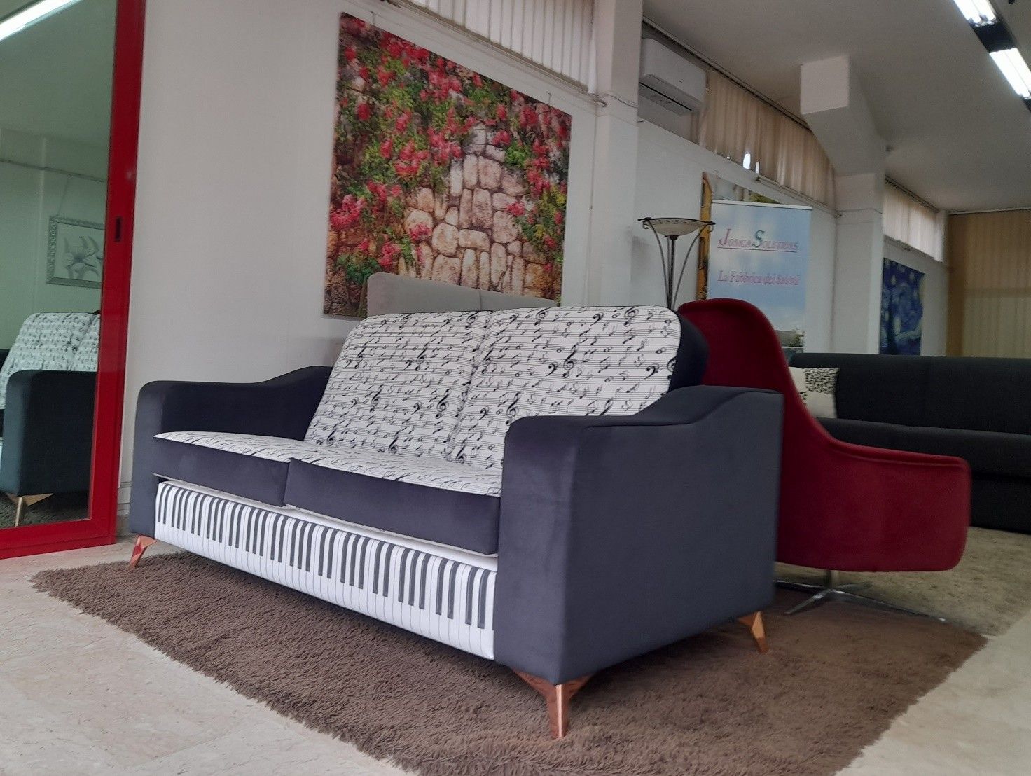 Divano con disegno di tasti di pianoforte sulla parte anteriore e note musicali sui cuscini, in uno showroom.