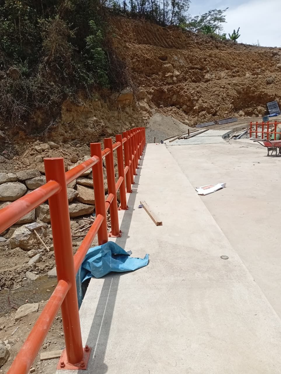 Barandilla naranja a lo largo de un camino de hormigón junto a una ladera de tierra.